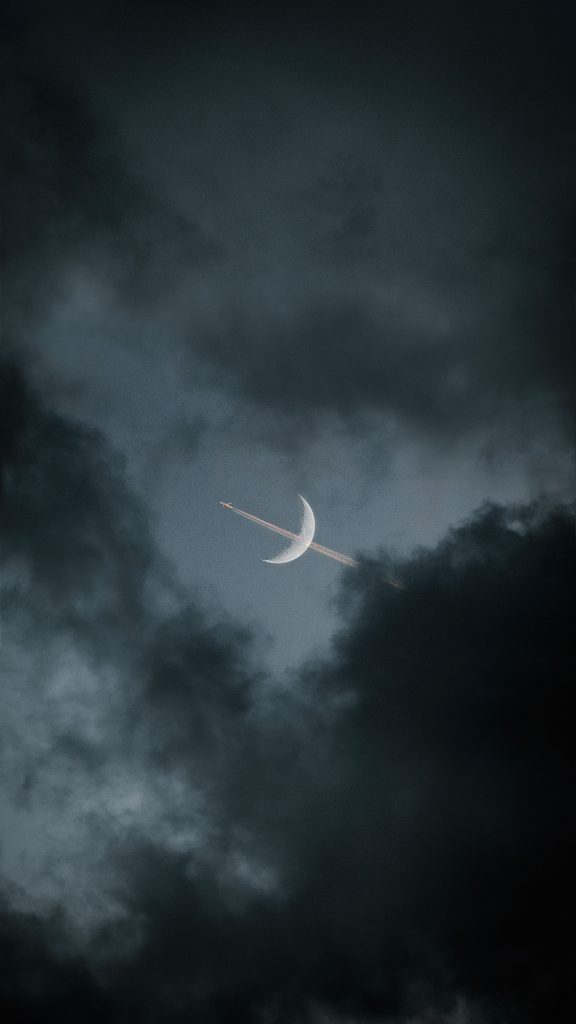 image of a jetliner bisecting the quarter moon in a night sky