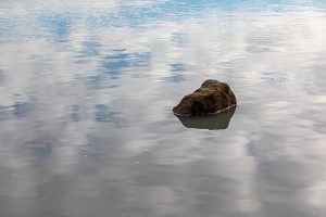 image of rock surrounded by reflection of clouds in the sea
