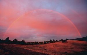 Photo of rainbow in a red, sunset sky.