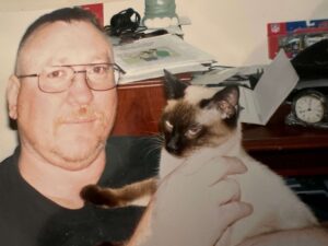 Tom cuddling a seal point Siamese cat.
